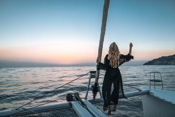 Woman in a flowing dress embracing the open sea breeze on a Santorini catamaran cruise at sunset.