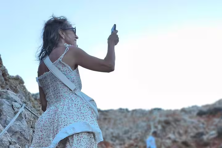 Woman capturing the breathtaking views of Seitan Limania beach on a sunny day, dressed in a floral dress.
