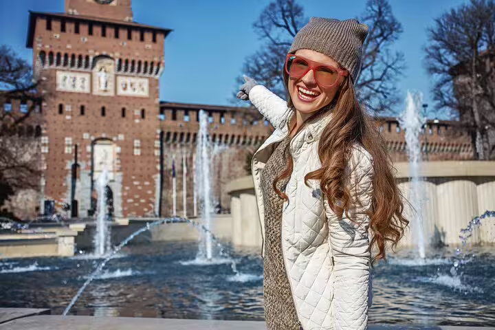 Smiling woman pointing at Sforza Castle in Milan on a sunny day, highlighting a private walking tour with gelato.