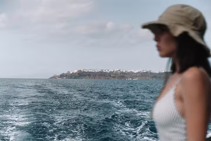 Silhouette of a woman gazing at Santorini's coastline from a catamaran on a serene private cruise.