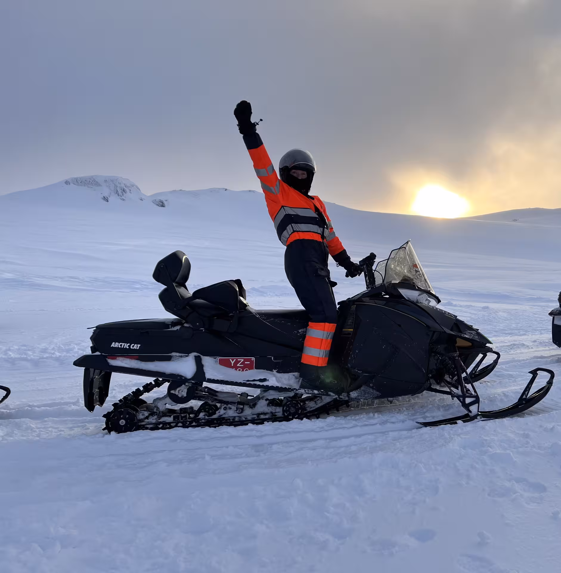 Woman celebrating on a snowmobile during a thrilling Icelandic winter sunset adventure, perfect for New Year's Eve fun.