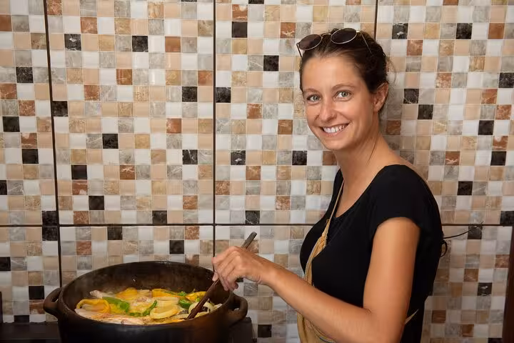 Woman happily stirring a traditional Bahian dish in a colorful tiled kitchen during a Salvador cooking class.