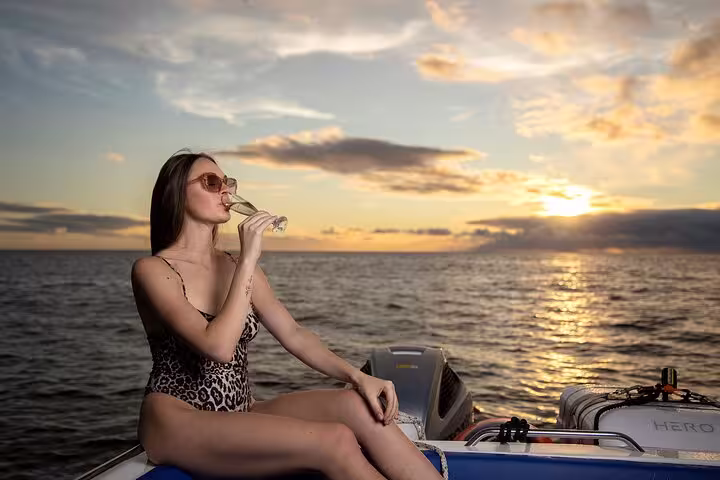 Woman relaxes with a drink on a boat, enjoying a stunning sunset over the ocean on a Desertas Island Tour.