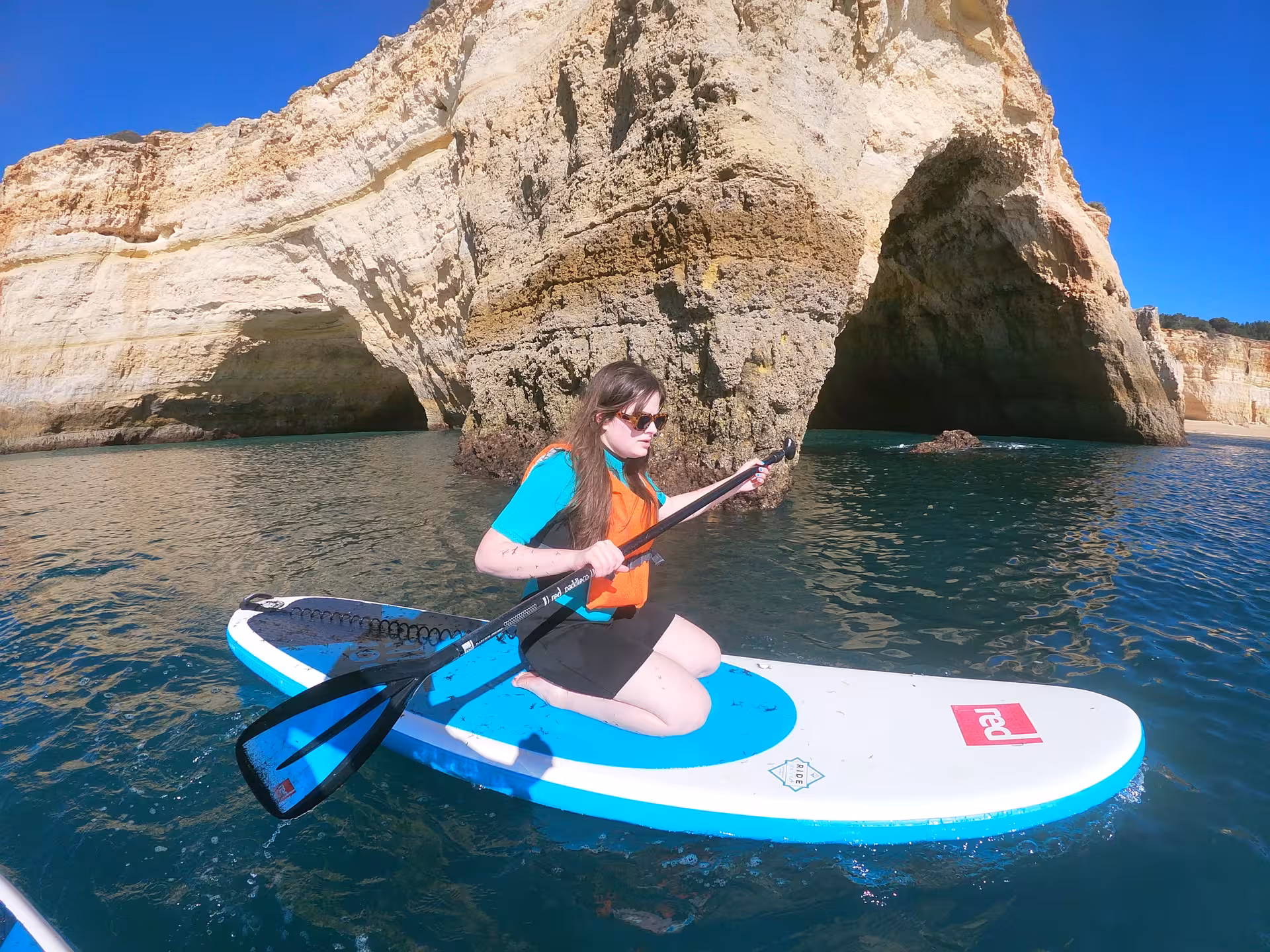Woman kneeling on a stand up paddle board exploring Algarve sea caves and golden cliffs on a sunny Benagil SUP tour