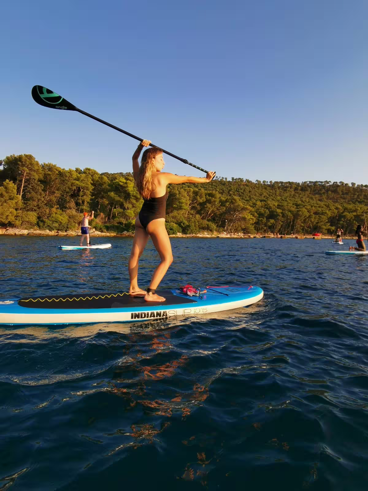 Woman stand up paddling on calm Adriatic Sea during morning SUP tour in Split, Croatia, with pine coast views