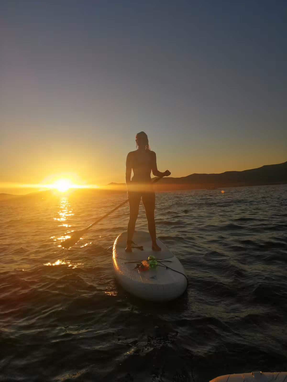 Woman standing on SUP at sunset off Split, Croatia, with paddle and wine on board during guided evening tour