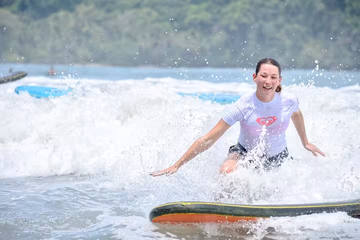Woman enjoying surf lesson in Manuel Antonio, skillfully riding a wave with lush greenery in the background.