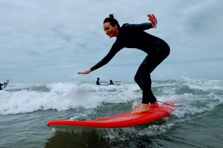 Woman surfing a wave on a red surfboard at Caparica Surf Experience, perfect for beginners and adventure seekers.