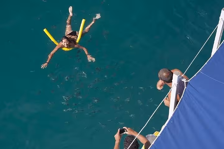Smiling woman swimming with a noodle near a boat while others capture the moment on a Paraty boat tour.