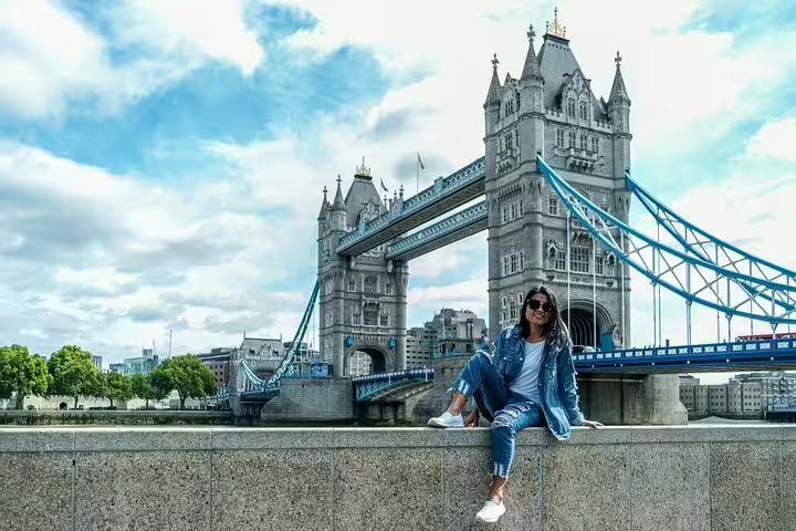Woman sitting by Tower Bridge in London, enjoying the scenic view on a private tour of Camden Town, downtown, and markets.