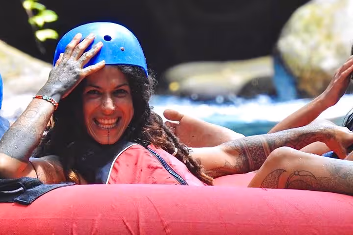 Smiling woman enjoying tubing adventure in Rio Celeste with a blue helmet and vibrant surroundings.