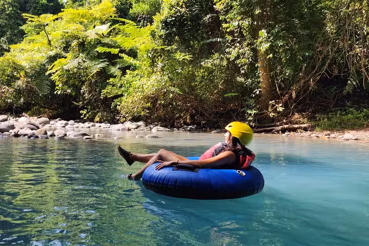Woman peacefully floats on a tube in the clear, blue waters of Rio Celeste surrounded by lush greenery.