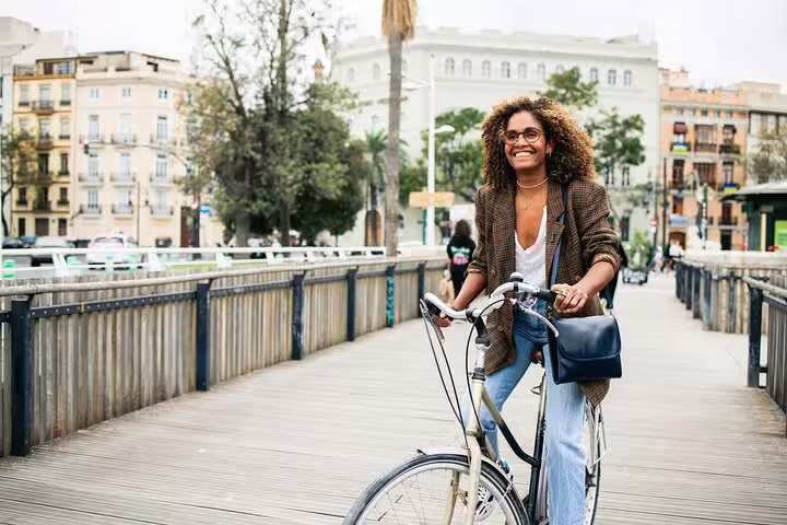 Woman enjoying a scenic Valencia bike tour on a wooden bridge, surrounded by historic architecture and vibrant city views.