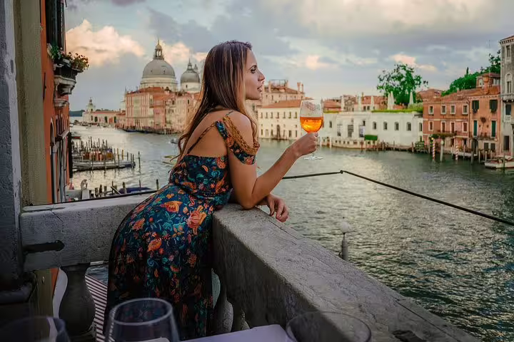 Woman savoring a drink on a Venetian balcony overlooking the Grand Canal, capturing the essence of Venice's charm and beauty.