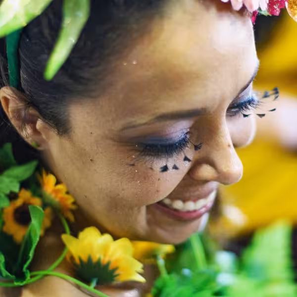 Close-up of a smiling woman in vibrant floral costume at a lively carnival street party.