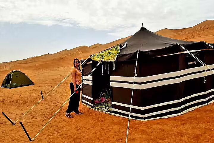 Woman standing next to a traditional desert tent in the vast landscape of Wahiba Sands on a private tour from Muscat.