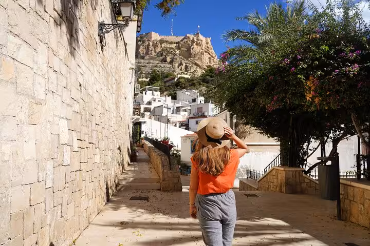 Woman walking towards Santa Bárbara Castle under clear skies during a private city tour in Alicante.