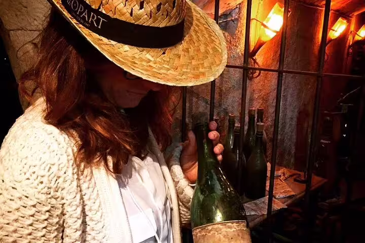 Woman in a straw hat examining a wine bottle in a dimly lit cellar during a Montserrat & Winery tour experience.