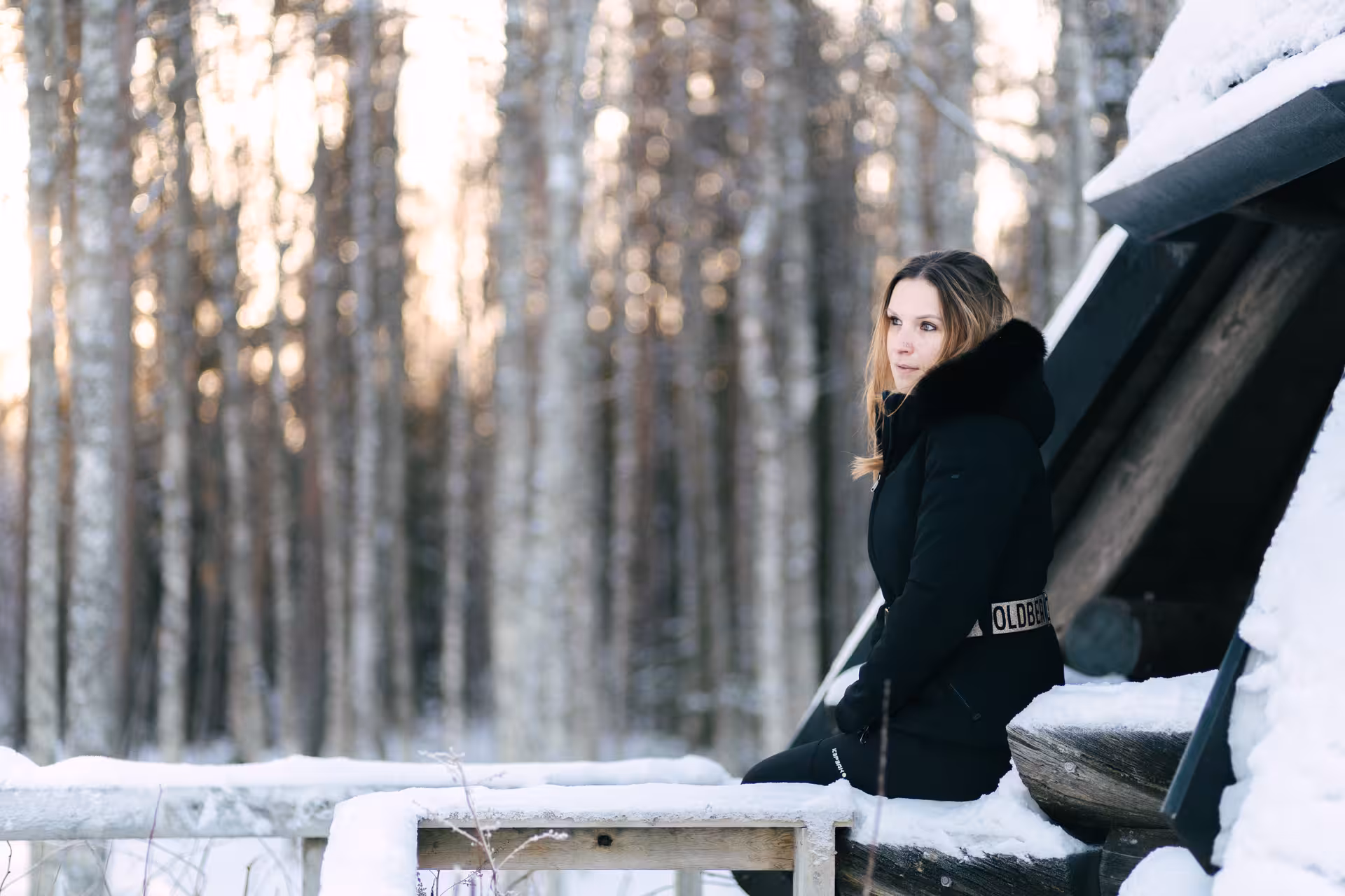 Woman in a black coat enjoys a serene winter moment in a snowy Rovaniemi forest setting.