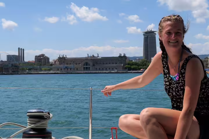 Smiling woman on a yacht enjoying a sunny day with Barcelona skyline in the background, perfect for a sunset cruise adventure.