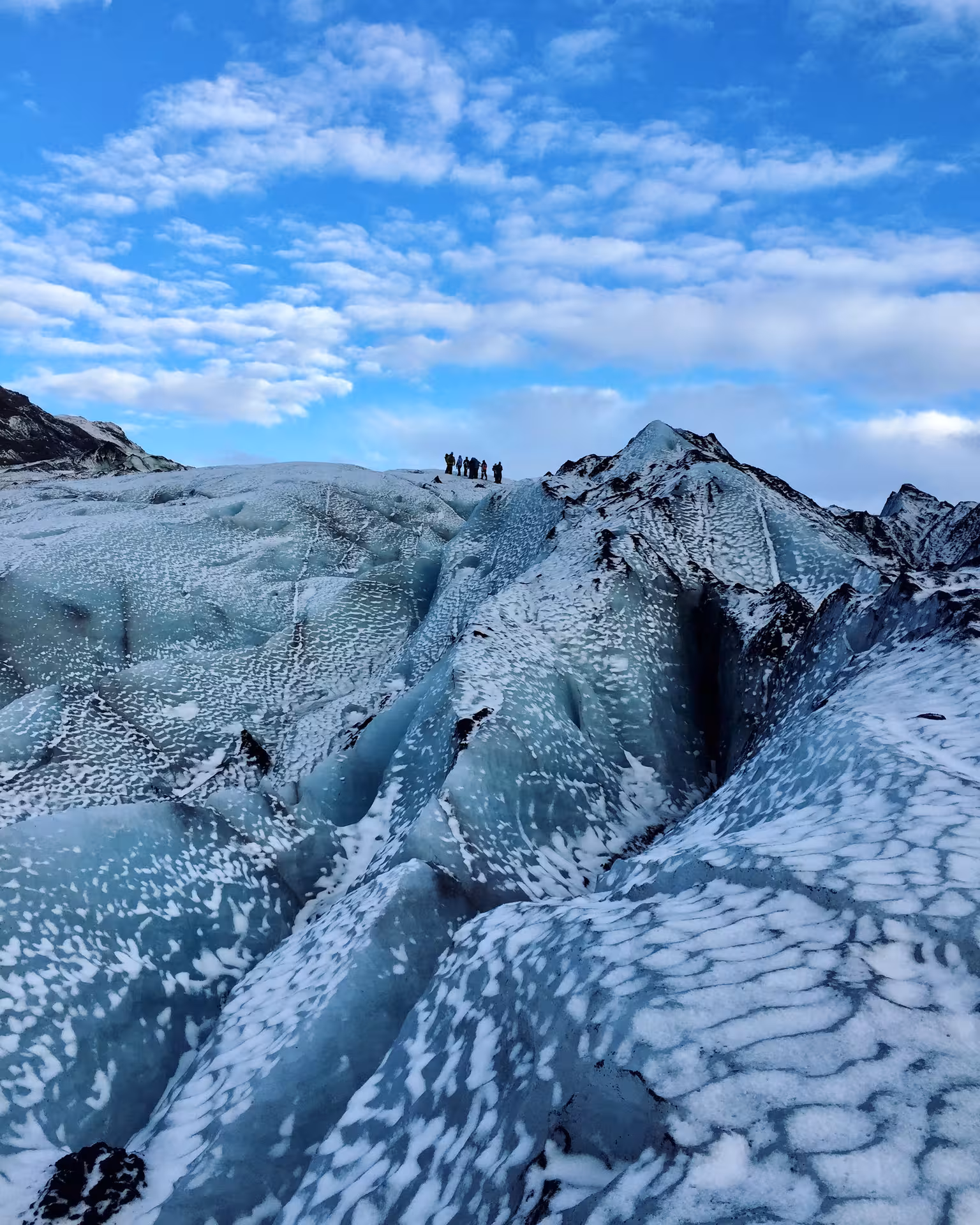 Women exploring the icy expanse of a glacier under a bright blue sky on an Iceland adventure tour.