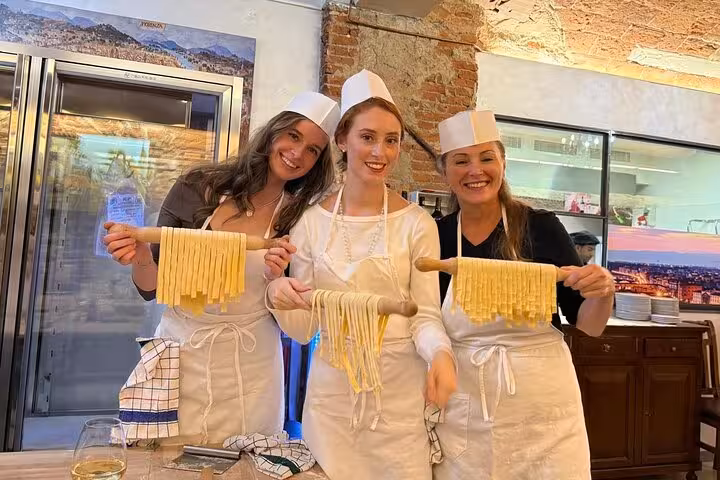 Three women proudly display their freshly made pasta during a cooking class in Florence's culinary studio.