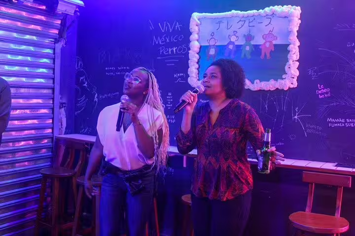 Two women singing karaoke in a vibrant São Paulo bar during a lively pub crawl night.