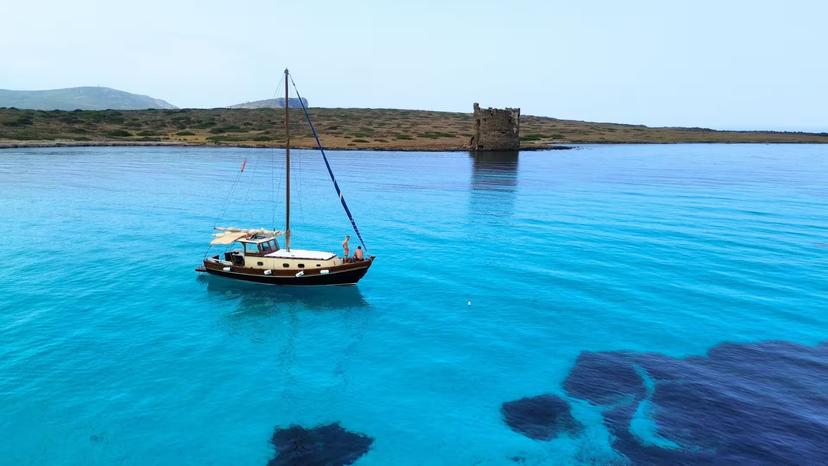 Wooden boat sailing near Asinara Island's clear blue waters and ancient tower, part of Stintino tour.