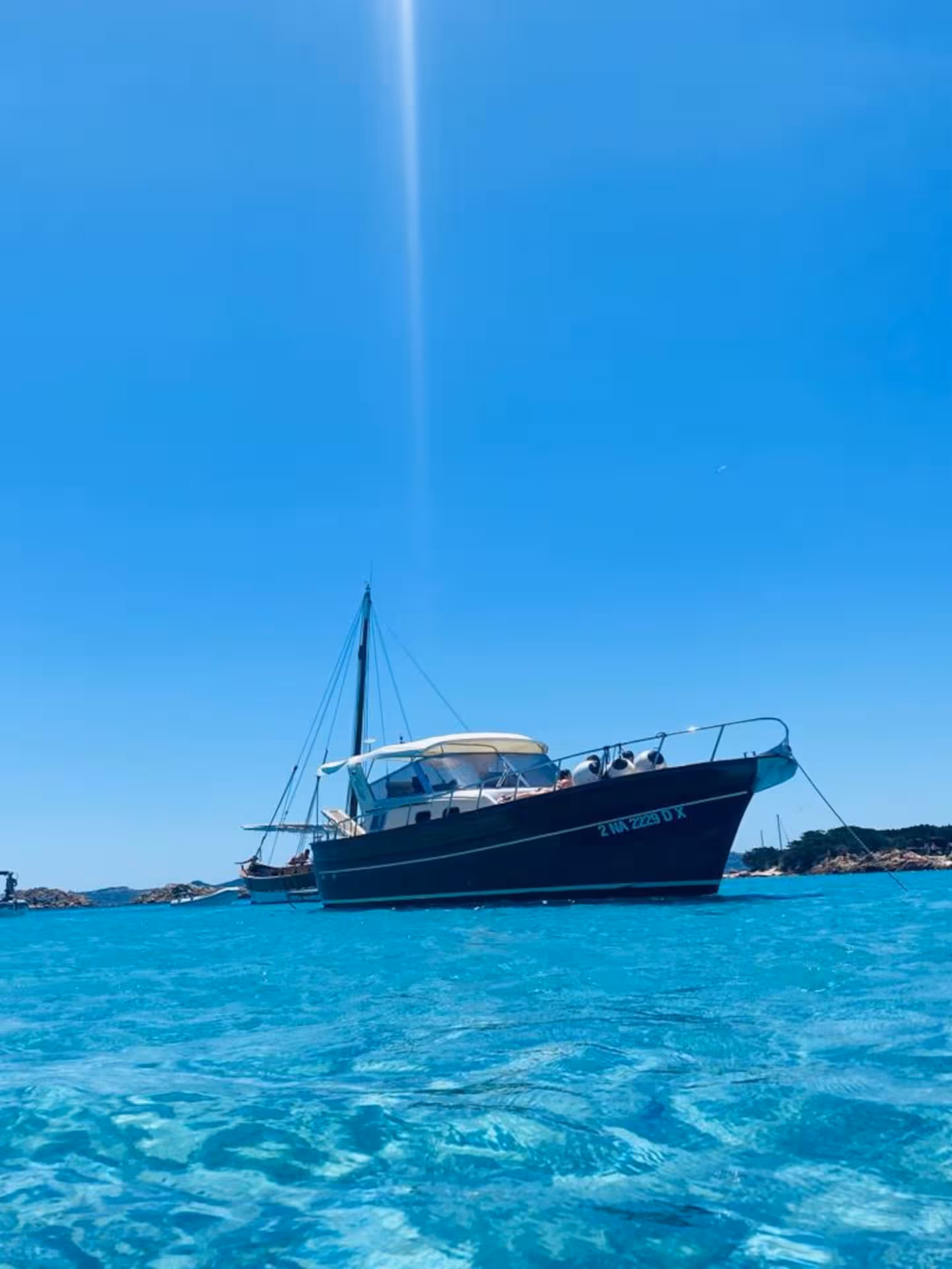 Wooden boat anchored in crystal-clear waters under a bright blue sky in southern Corsica.