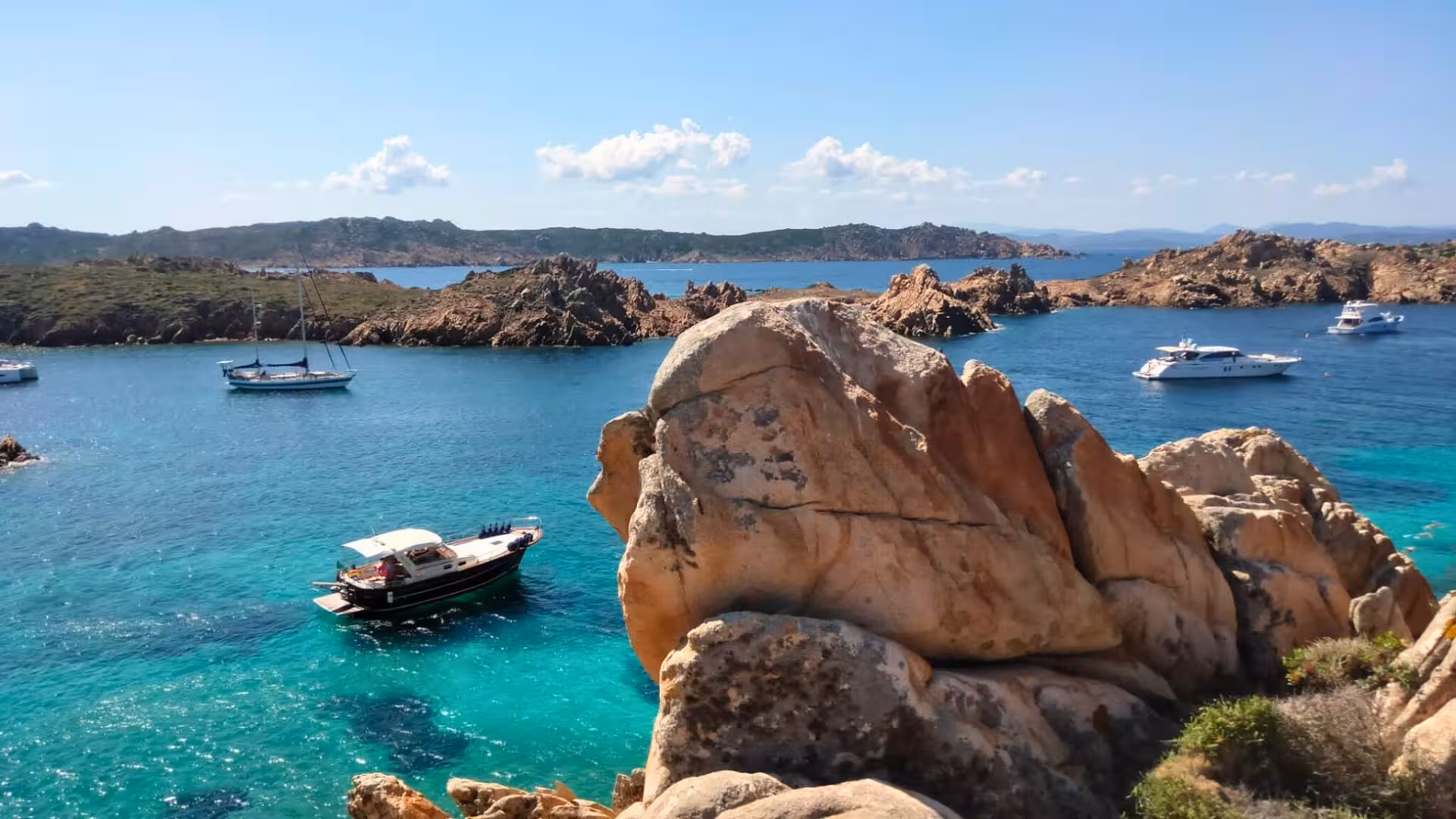 Wooden boat anchored in turquoise waters near rugged cliffs in La Maddalena, ideal for Corsica boat tours.