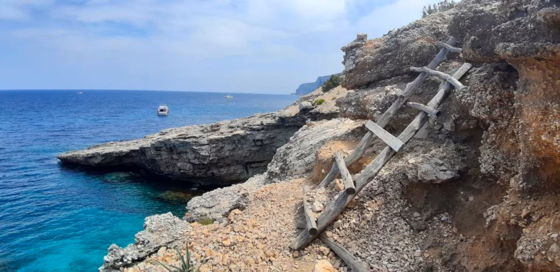 Rustic wooden ladder on rocky cliffside overlooking Cala Mariolu's turquoise waters in Baunei, Sardinia.