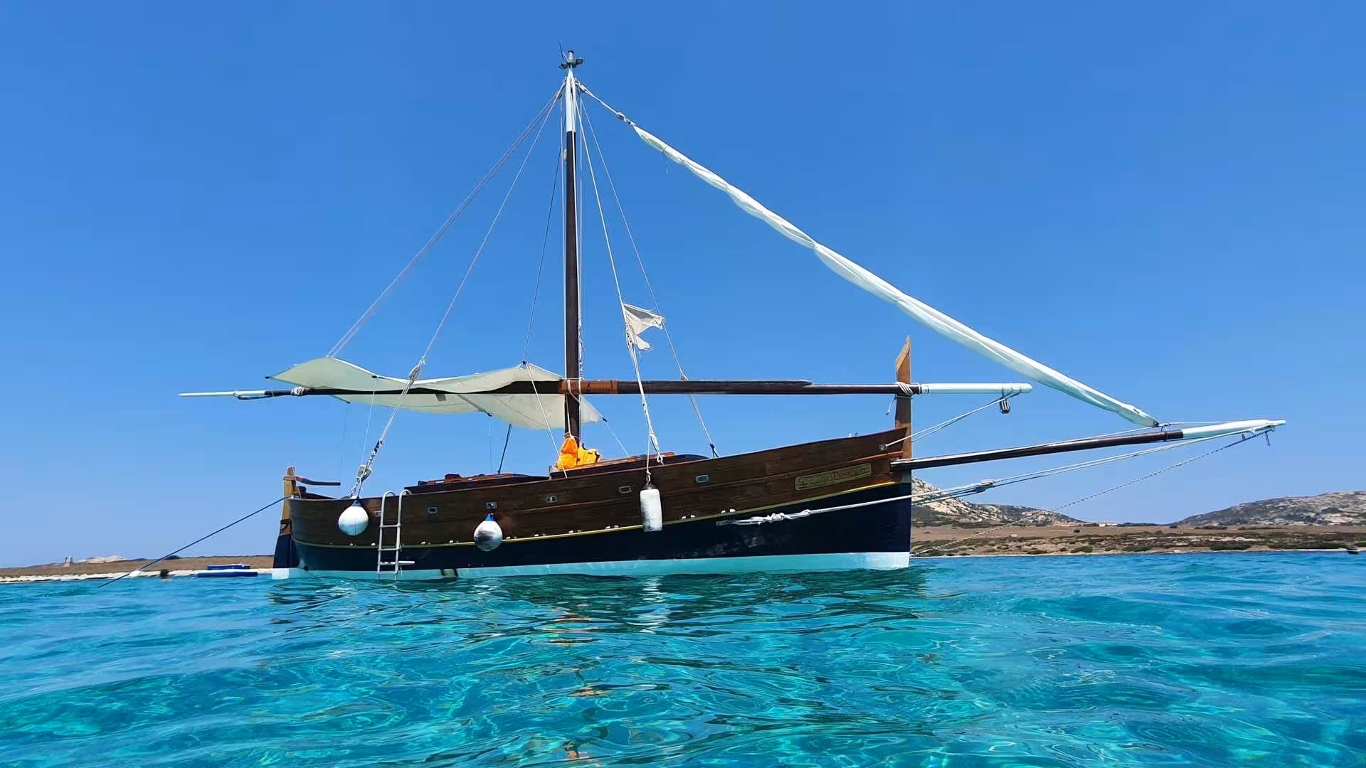 A classic wooden sailboat anchored in clear blue waters, showcasing the beauty of the Stintino to Asinara sailing tour.