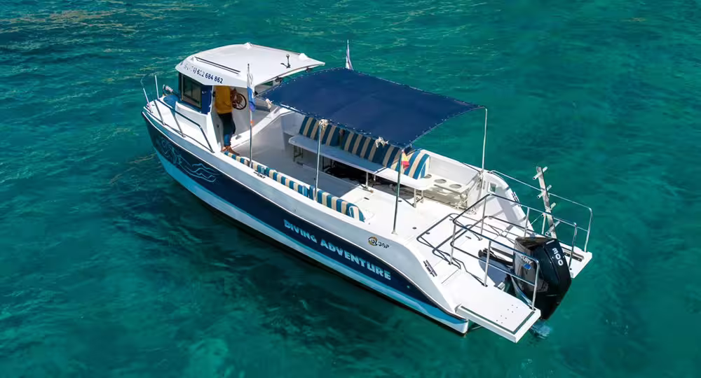 Aerial view of a modern diving boat with shaded seating, set against clear turquoise waters for the Wreck Corveta Afonso Cerqueira tour.