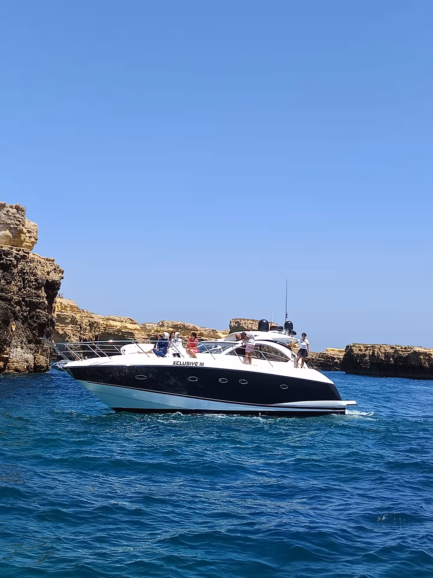XCLUSIVE III Private Luxury Yacht sailing past rocky Algarve coastline in clear blue water with happy guests on board