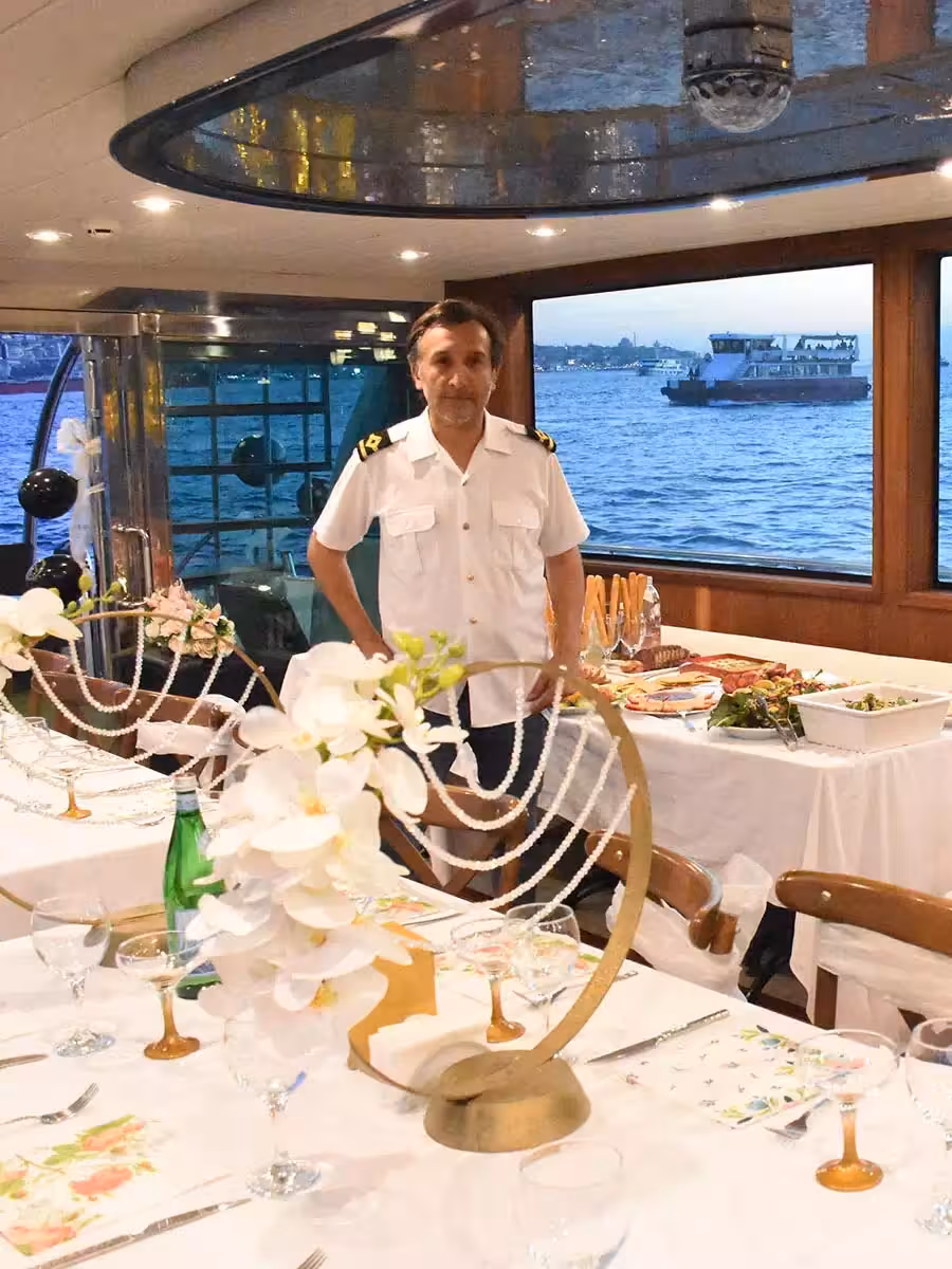 Captain beside decorated tables and buffet on a yacht birthday party cruise with ocean views through windows