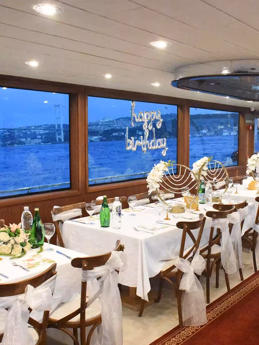 Elegant indoor dining setup for a yacht birthday party with Happy Birthday decor and Bosphorus evening views