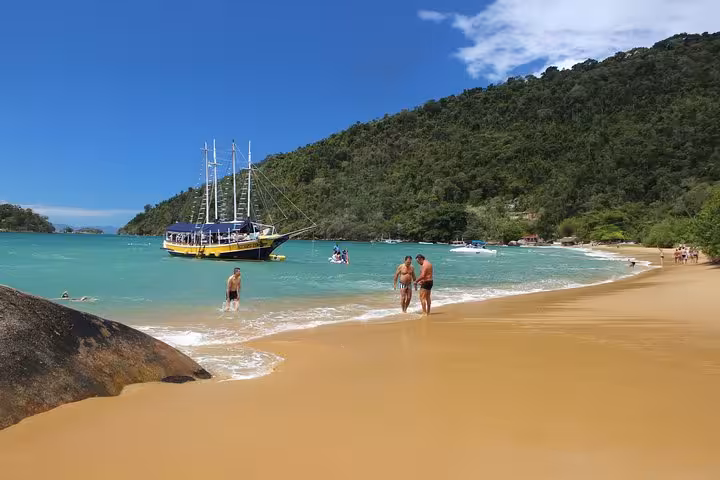 Scenic boat tour featuring a yellow vessel near a lush green island and sandy beach under a clear blue sky.