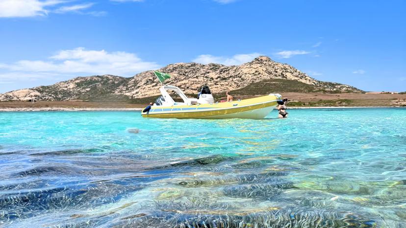 Yellow dinghy floating on crystal-clear waters near Asinara Island, showcasing vibrant marine life and scenic landscapes.