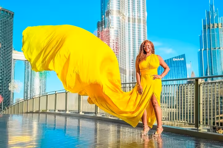 Radiant woman in a bright yellow dress with a billowing train, standing before the Burj Khalifa, capturing Dubai's glamour.