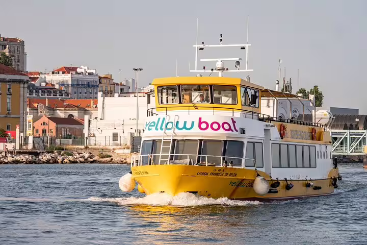 Yellow ferry cruising on Tagus River, Lisbon, during a food and drink private tour to Cacilhas, showcasing vibrant cityscape.