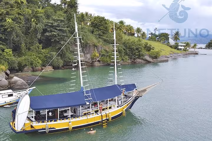Yellow schooner anchored in a tropical bay, offering standup paddle and kayak services amidst lush greenery.