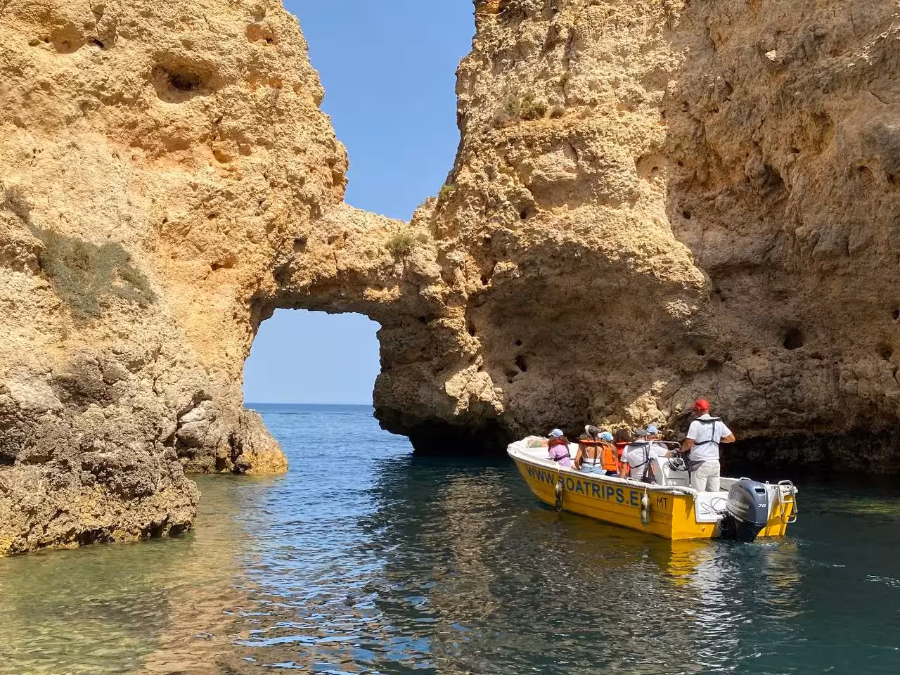 Yellow speedboat glides past Ponta da Piedade sea arch on Algarve express grotto tour from Lagos