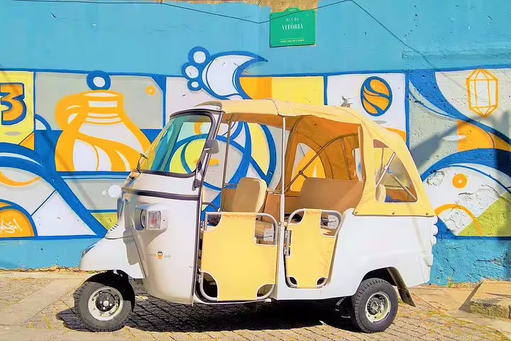 Bright yellow tuk tuk parked in front of colorful street art in Porto, offering a vibrant full-day private city tour experience.