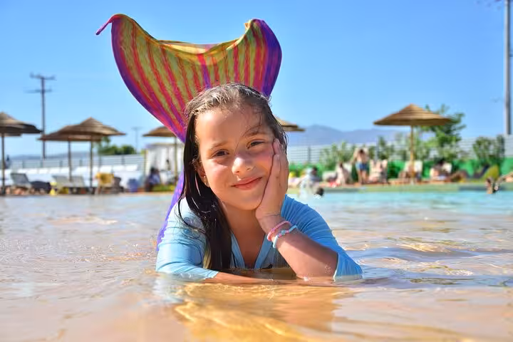 Young girl with a colorful mermaid tail posing happily in a pool during a Hersonissos photoshoot experience.