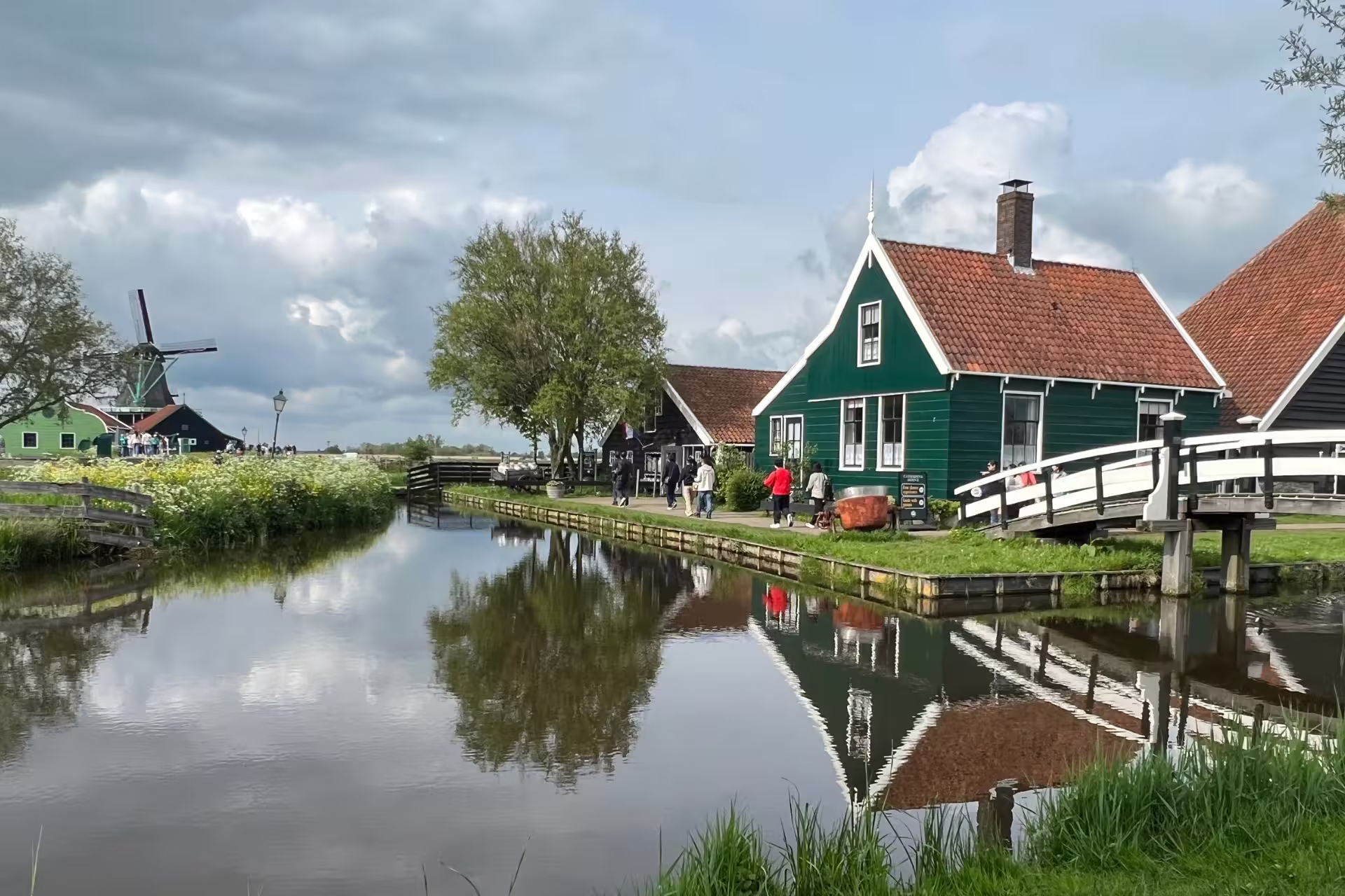 Zaanse Schans canal with green wooden house, footbridge and windmill, classic Amsterdam day trip scenery
