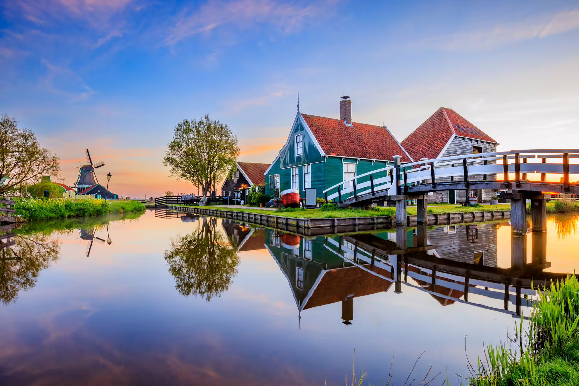 Sunset canal view with green Zaanse Schans houses, bridge and windmill, perfect for 1-day audioguide walk
