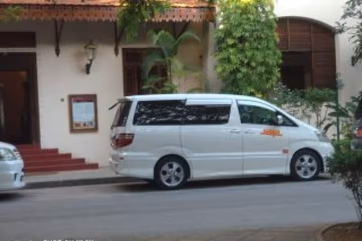 White minivan parked outside a hotel, ideal for 24/7 private airport transfers to Nungwi Hotels in Zanzibar.