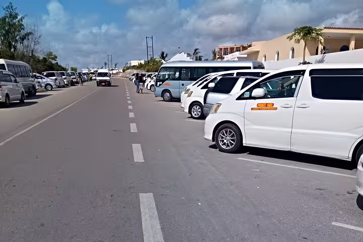 Row of private transfer vans at Zanzibar Airport, ready for hotel transportation under a clear blue sky.