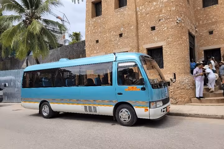 Stylish blue minibus parked near historic building for Zanzibar airport transfer service.