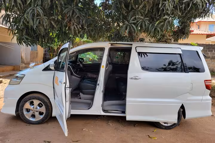 Comfortable interior of white airport transfer van with open doors, ready for 24/7 service to Nungwi hotels, Zanzibar.